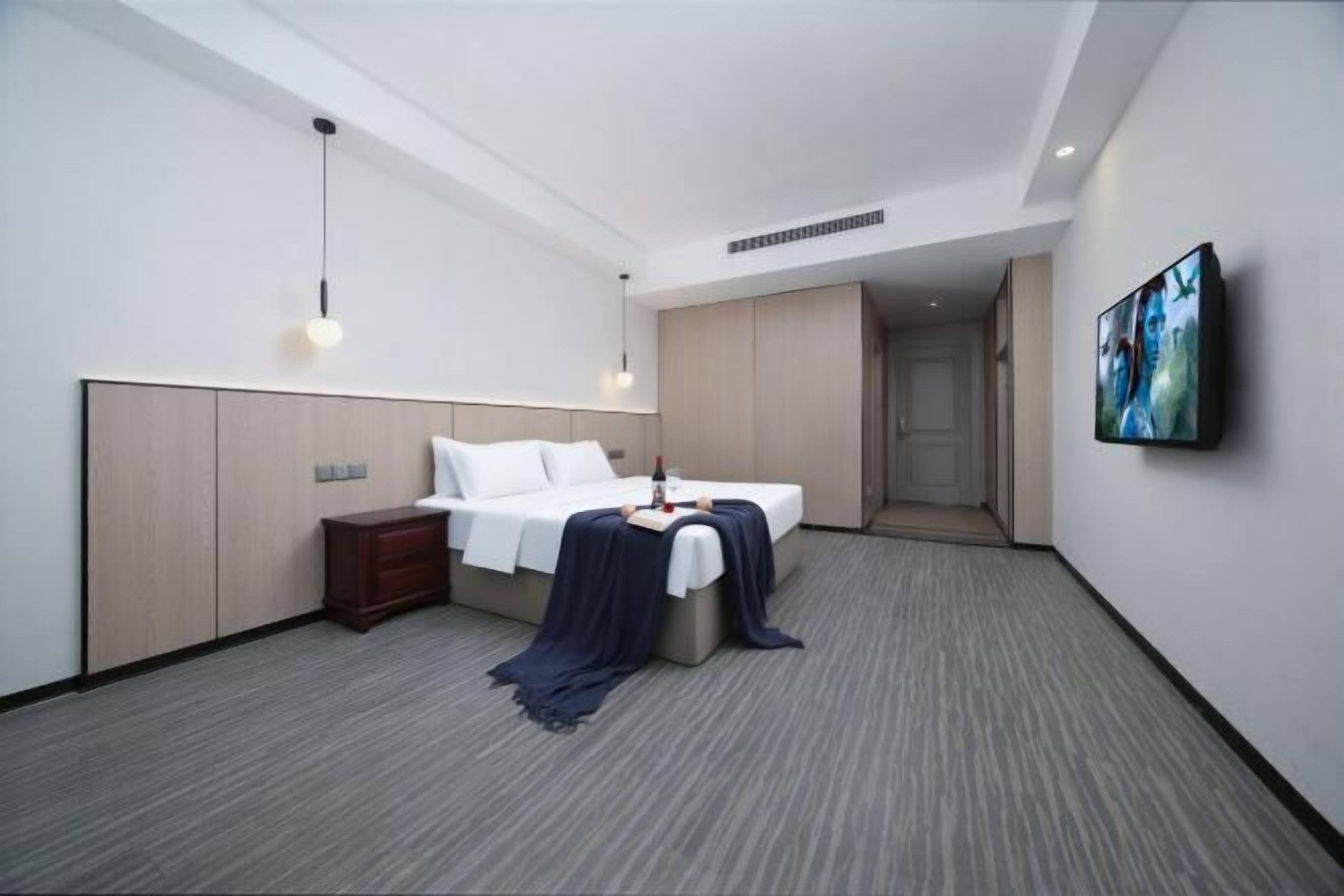 A modern hotel room with a bed, bedside table, TV, and a walk-in closet.