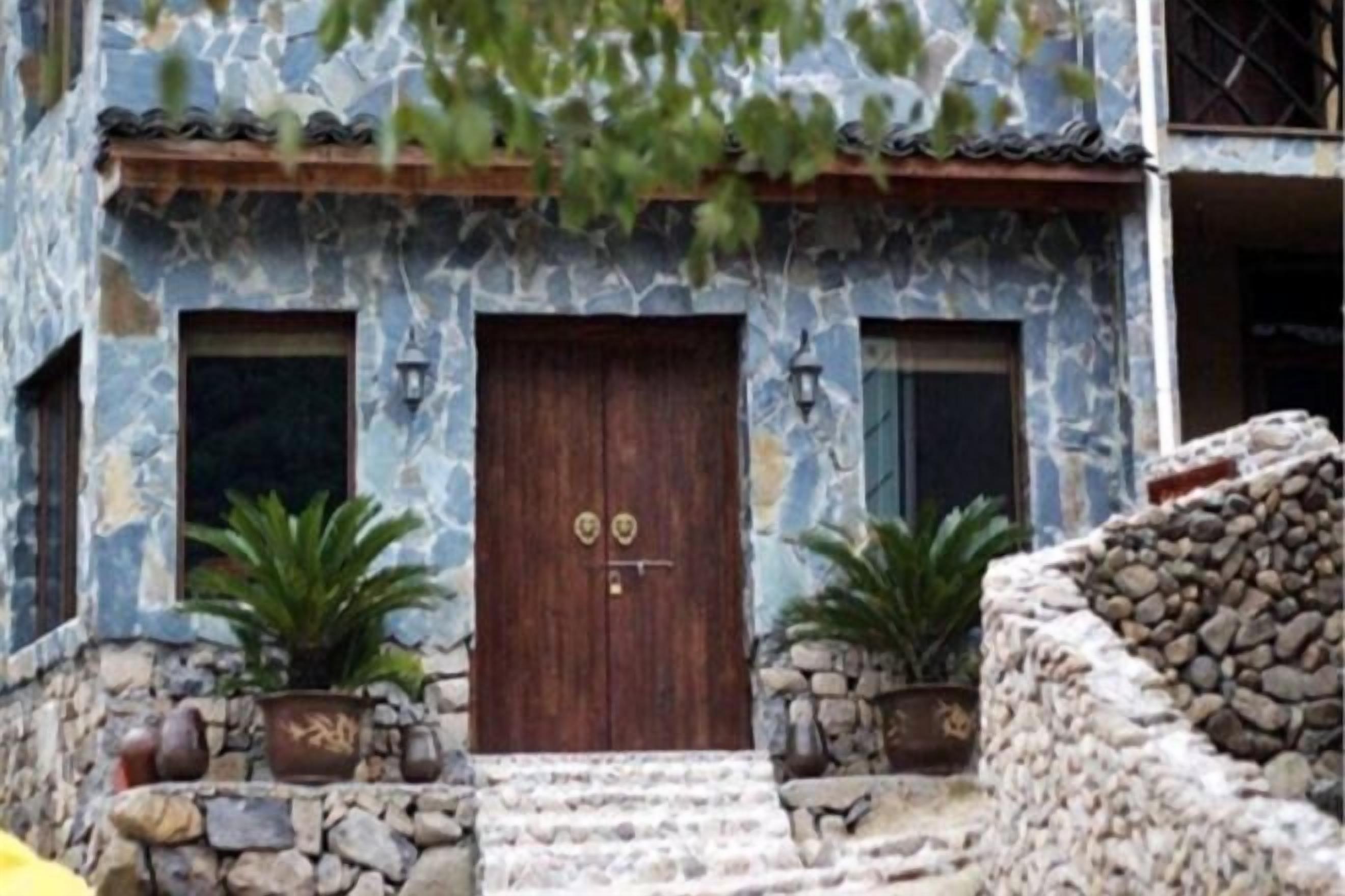 A stone facade with a wooden door, potted plants, and a stone wall.