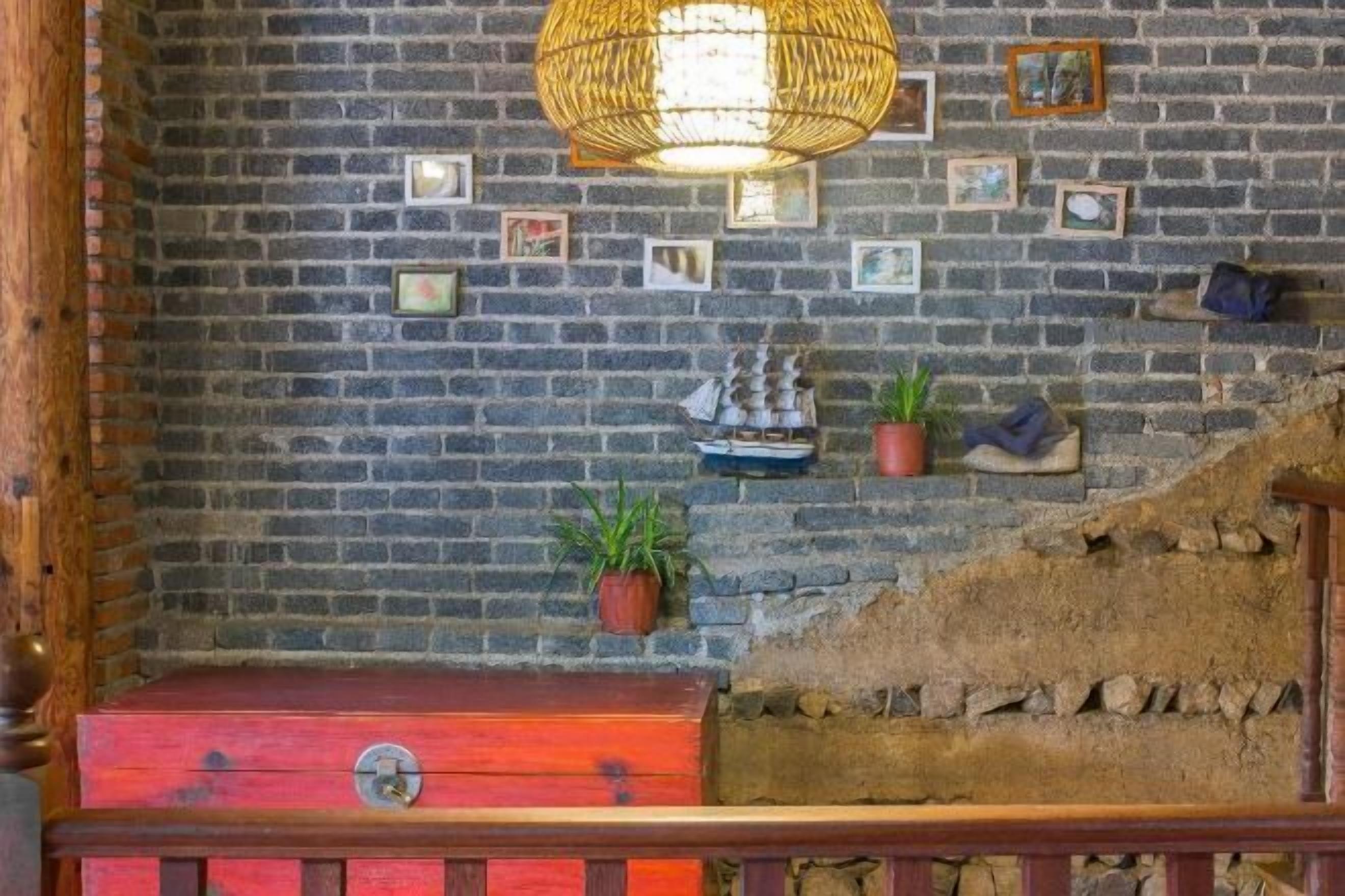 A room with a brick wall, a wooden bench, a red chest, a wicker lamp, and a small ship decoration.