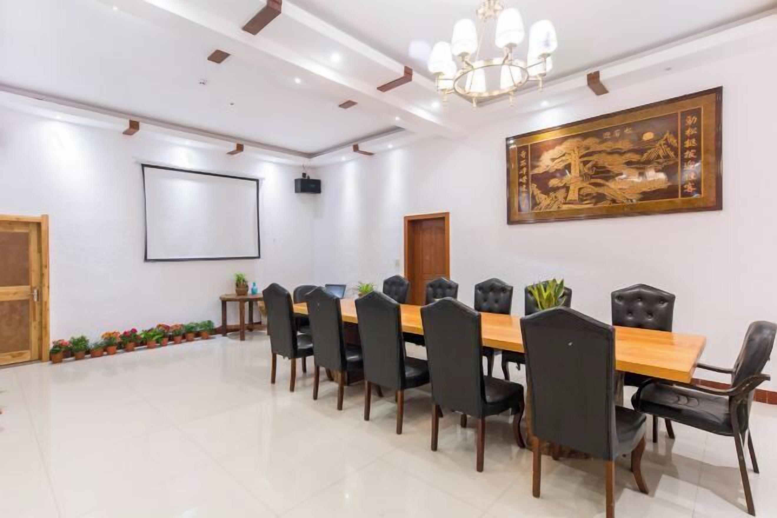 A conference room with a long table, black chairs, a projector screen, and a traditional artwork on the wall.