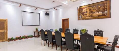 A conference room with a long table, black chairs, a projector screen, and a traditional artwork on the wall.