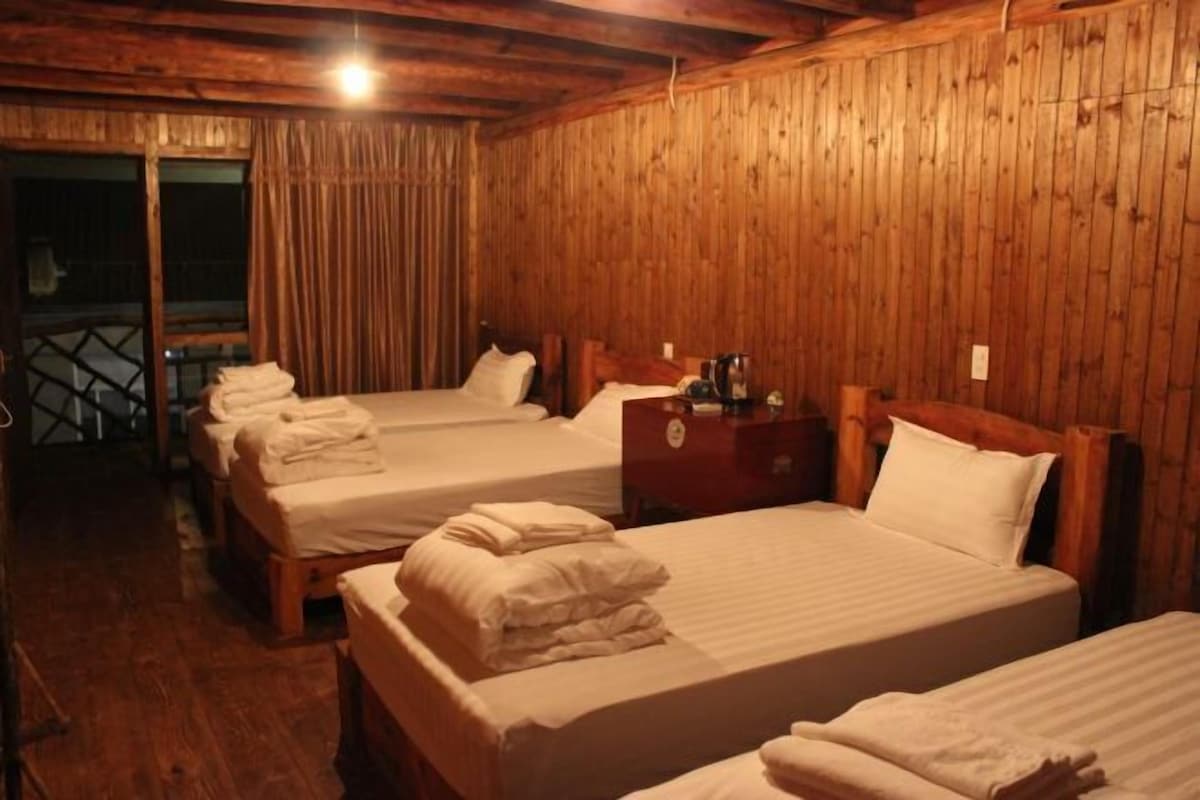A room with wooden walls and floors, featuring three beds with white linens and towels.