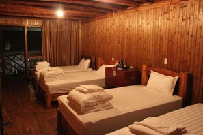 Una habitación con paredes y suelos de madera, con tres camas cubiertas con ropa de cama y toallas blancas.