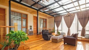 Ein geräumiger Wohnbereich mit Holzboden, Glasdecke und großen Fenstern mit Vorhängen.