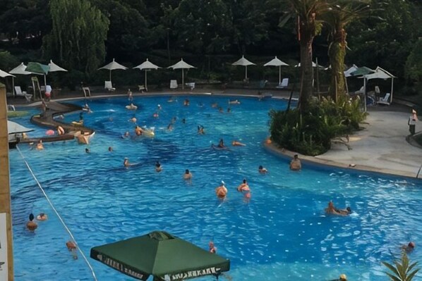 Une piscine où se trouvent plusieurs personnes, entourée de parasols et de chaises longues.