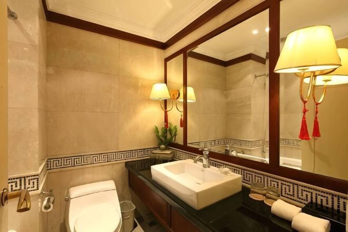 A bathroom with a large mirror, a sink, a toilet, and a towel rack.