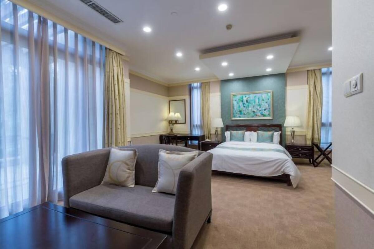 A hotel room with a bed, a sofa, a desk, and a large window with curtains.