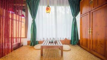 A room with a wooden floor, a table with a hanging light, green curtains, and a wooden wardrobe.