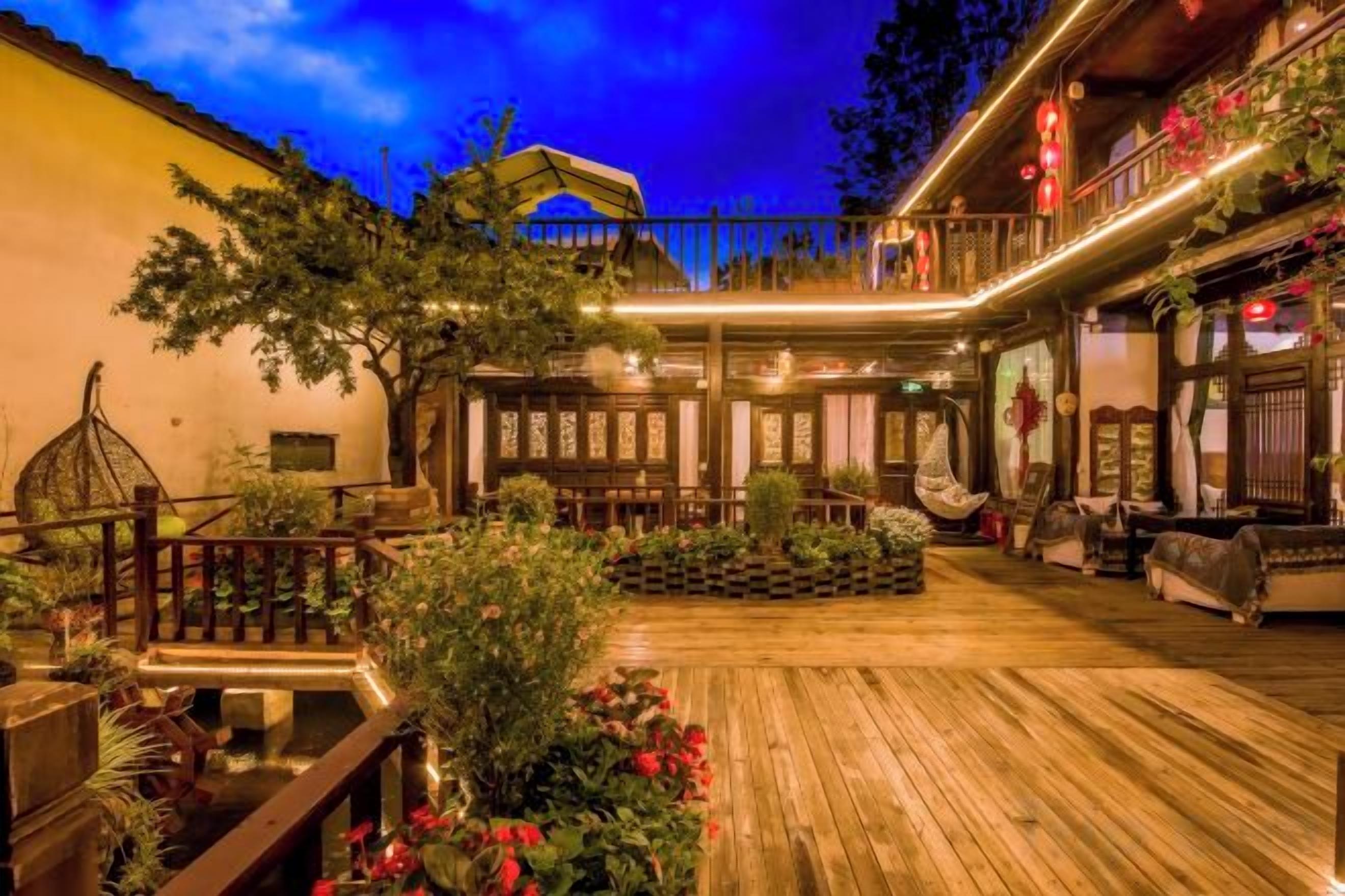 Un edificio de estilo tradicional con terraza de madera, mobiliario exterior y plantas decorativas.