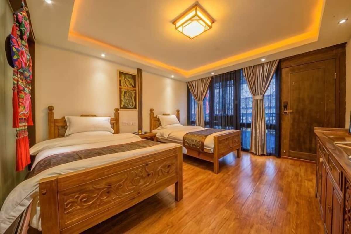 A hotel room with two wooden beds, a wooden bench, a large mirror, and a wooden wardrobe.