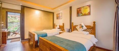 A hotel room with two wooden beds, a wooden desk, and a sliding glass door leading to an outdoor area.