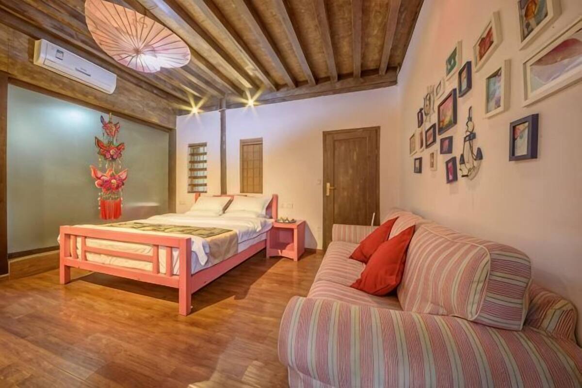 A bedroom with a wooden ceiling, a bed, a nightstand, a striped sofa, and a wall with framed pictures.