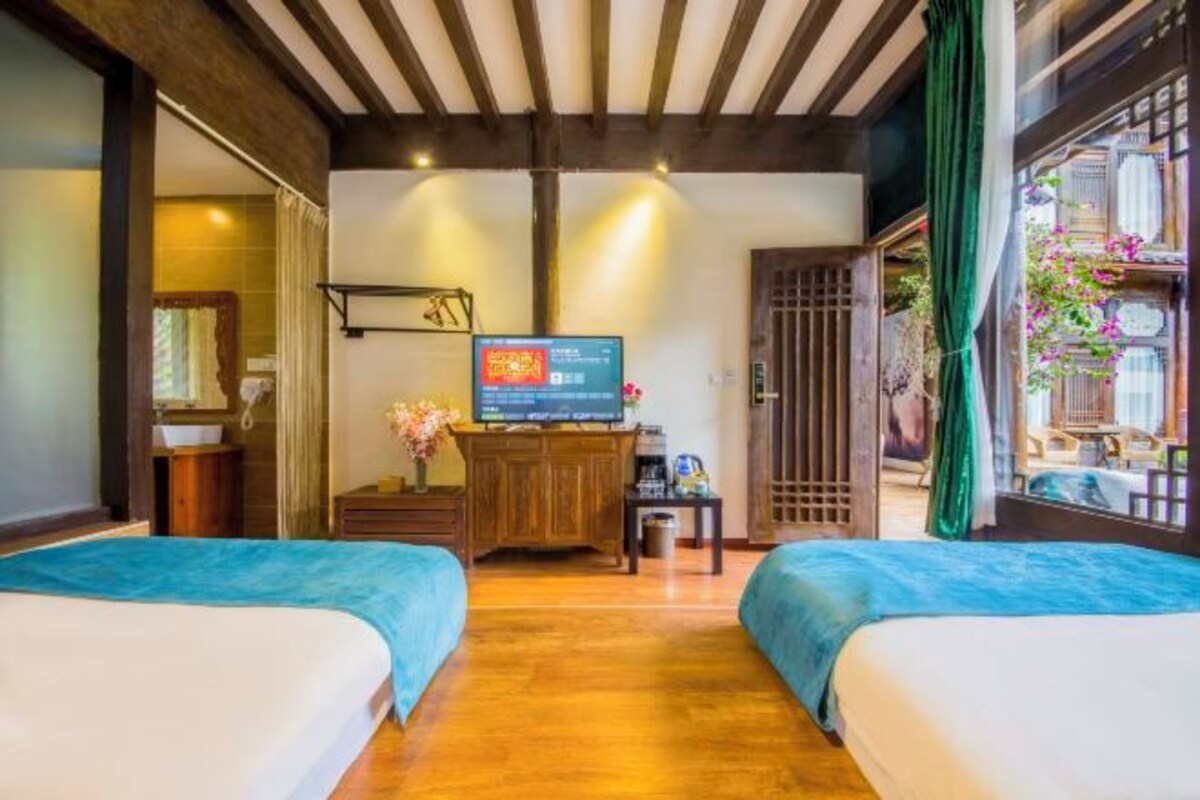 Una camera d'albergo con due letti, una televisione, un armadio in legno e una finestra con vista sull'esterno.