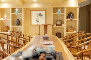 Une longue table en bois, entourée de chaises, un tableau encadré et des étagères ornées d’objets décoratifs.