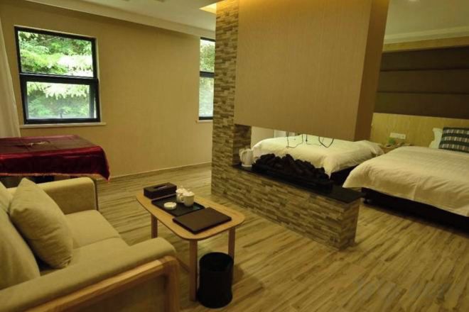 A hotel room with a bed, a sofa, a small table, and a window with a view of greenery.