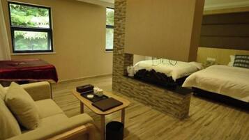 A hotel room with a bed, a sofa, a small table, and a window with a view of greenery.