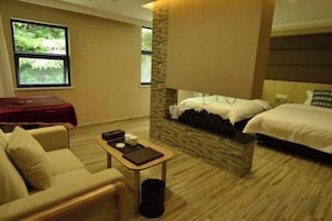 A hotel room with a bed, a sofa, a small table, and a window with a view of greenery.