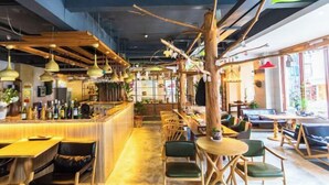 Et moderne restaurantmiljø med træbjælker, hængende pendellamper og en central træstamme.