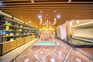 A hotel lobby with a central pool, wooden paneling on the ceiling, and glass display cabinets on the left. - Dexiju Hotel Shennongjia (Shennongjia)