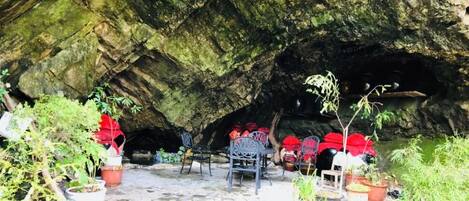 Interior de una cueva con piso empedrado, sillas y plantas en macetas.