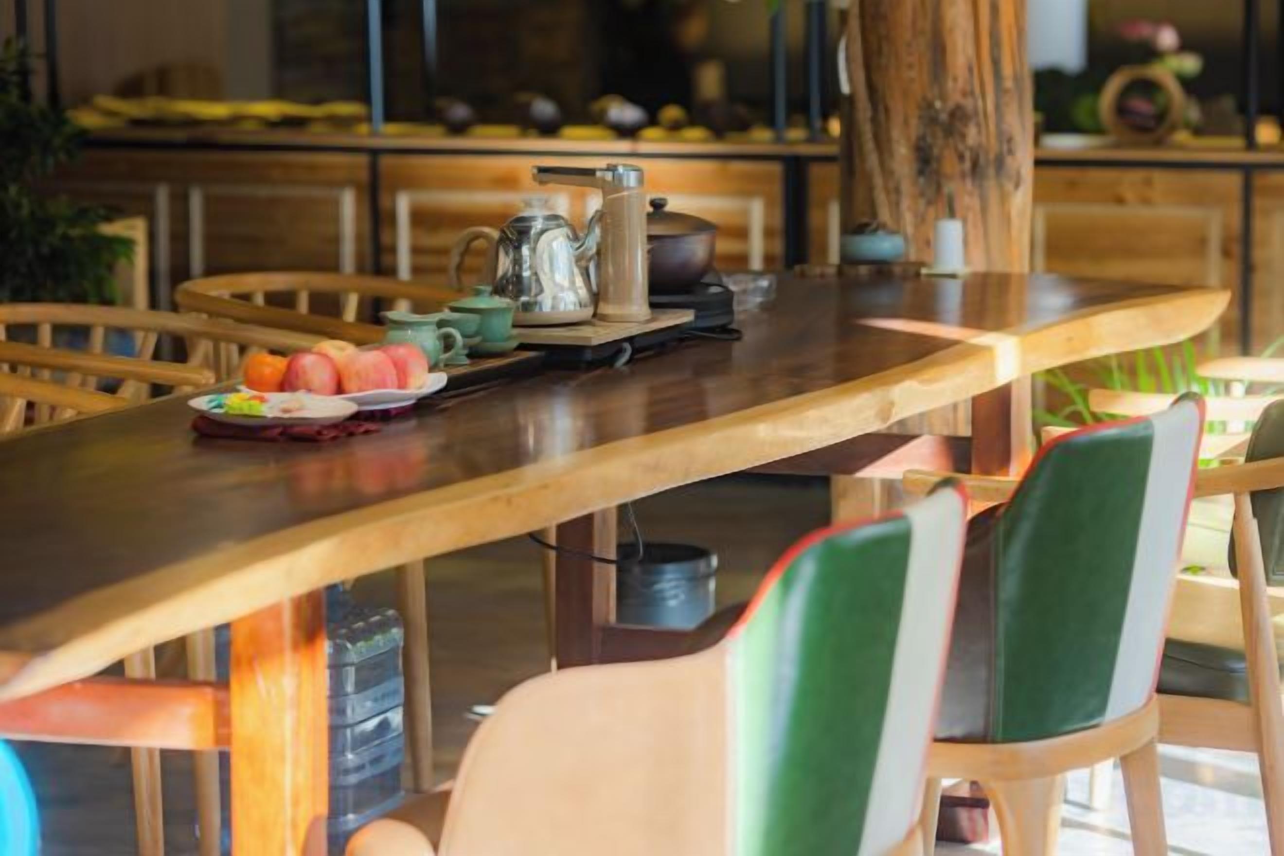 A wooden dining table with chairs, a pitcher, a teapot, and a plate of fruit.