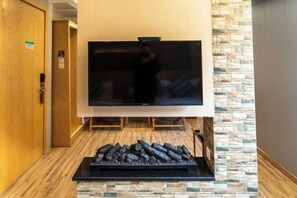 Hotellihuone, jossa on suuri, seinälle asennettu litteänäyttöinen televisio, puuovi ja kiviseinään upotettu takka, jossa palaa puita.