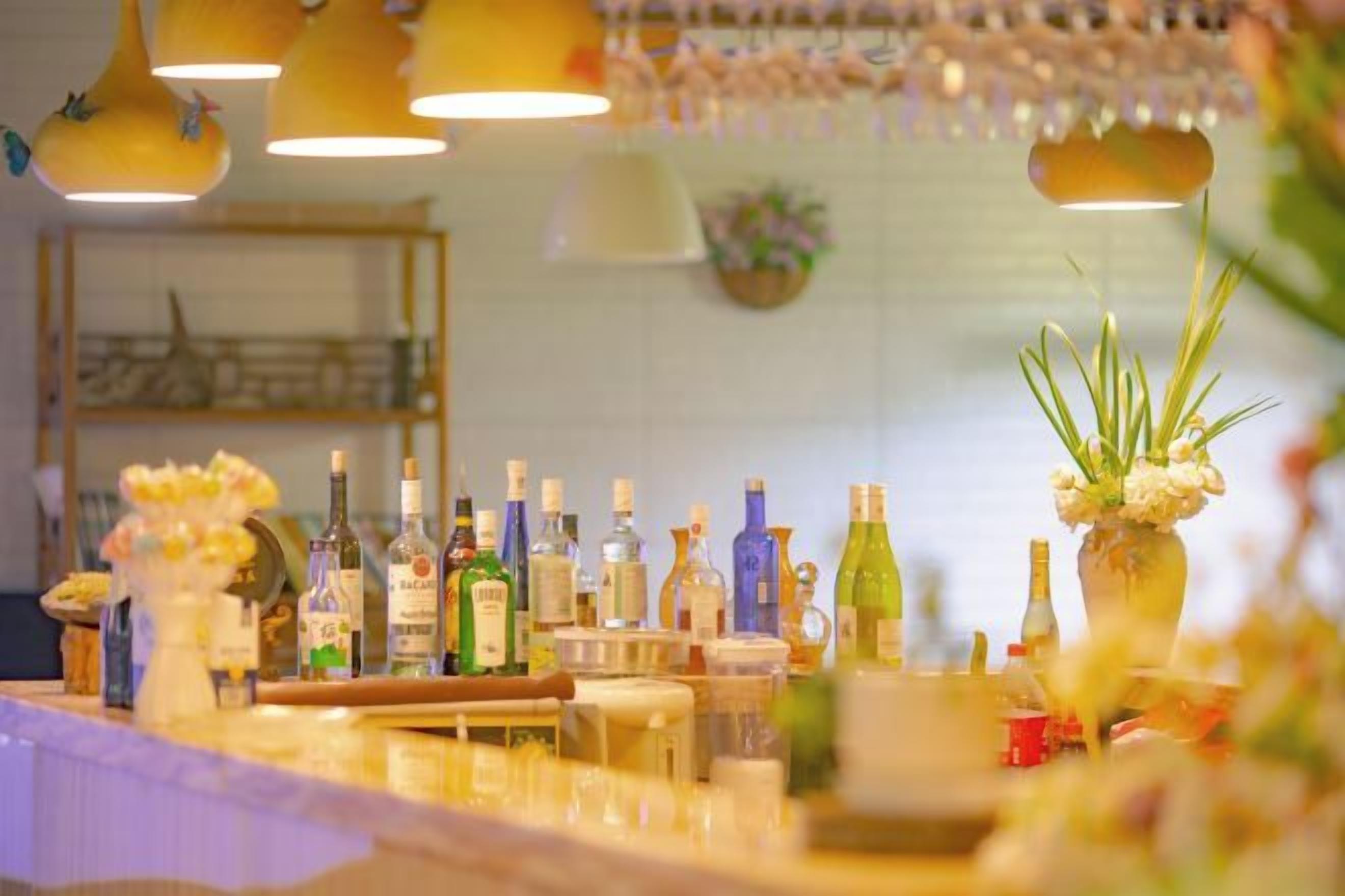 A bar area with various bottles and glasses, a wooden counter, and hanging lights.
