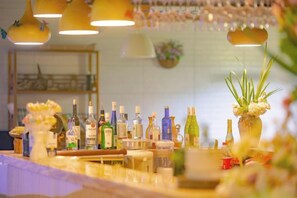Un espace bar avec diverses bouteilles et verres, un comptoir en bois et des luminaires suspendus.