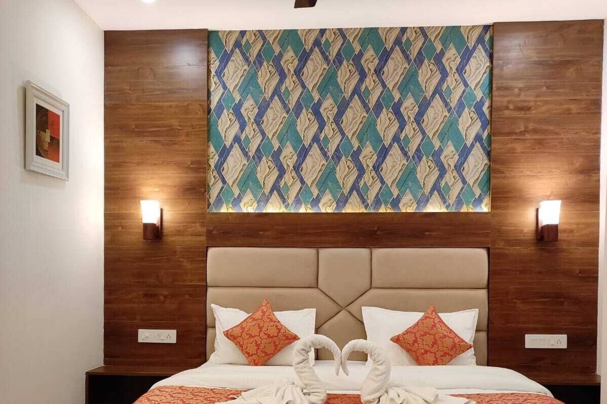Camera d'albergo con un letto grande, testiera in legno, decorazione murale a motivi e due lampade sui comodini, oltre a una ventola a soffitto.