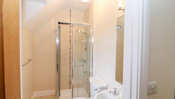 Un baño con ducha envuelta en vidrio, inodoro y lavamanos.