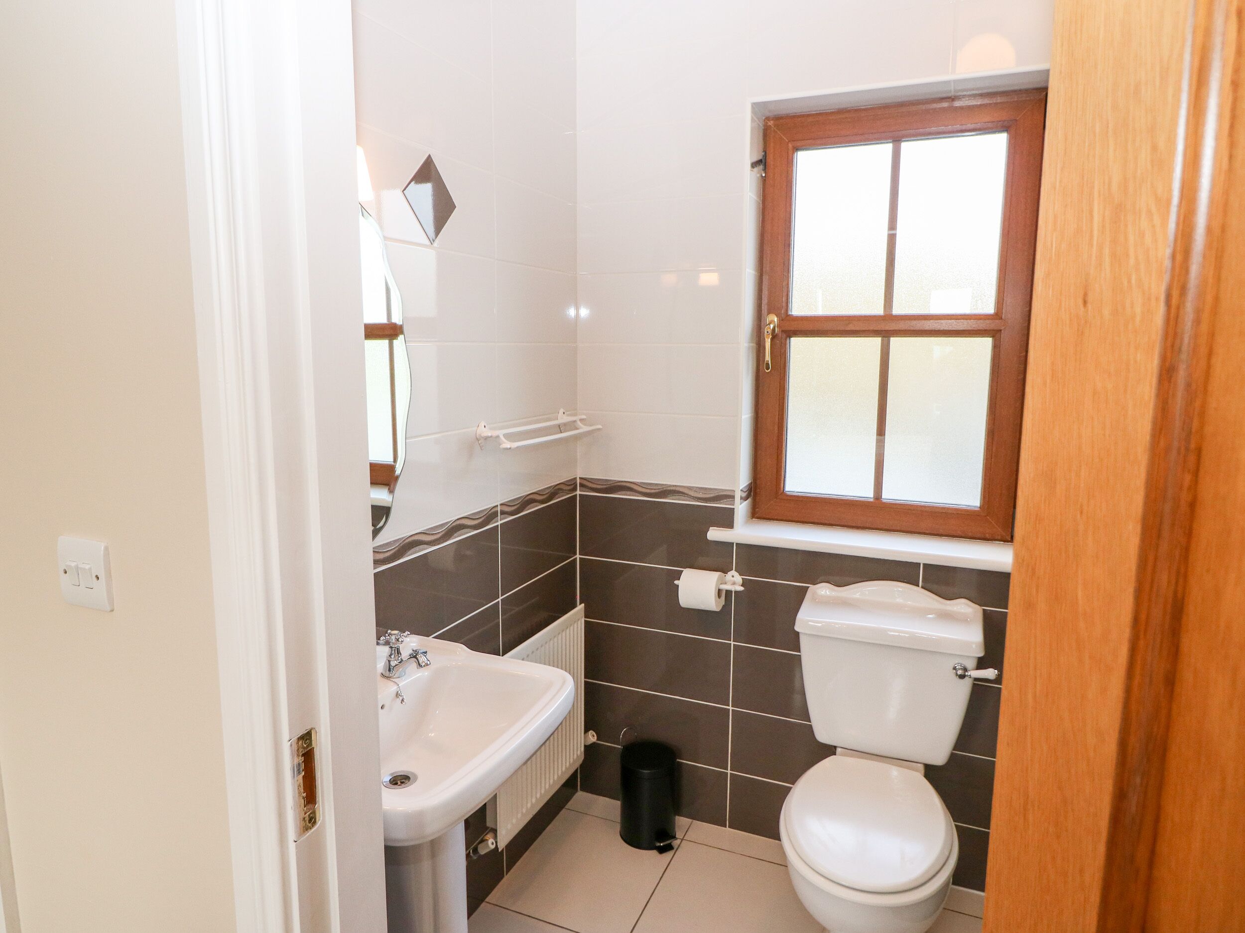 Un baño con lavamanos blanco, inodoro y ventana con marco de madera.