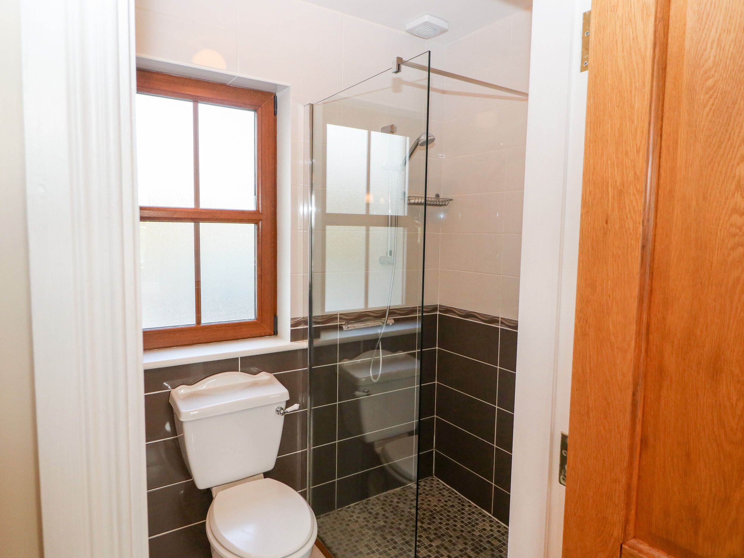 Ein Badezimmer mit Toilette, einer Duschkabine aus Glas und einem Fenster mit Jalousien.
