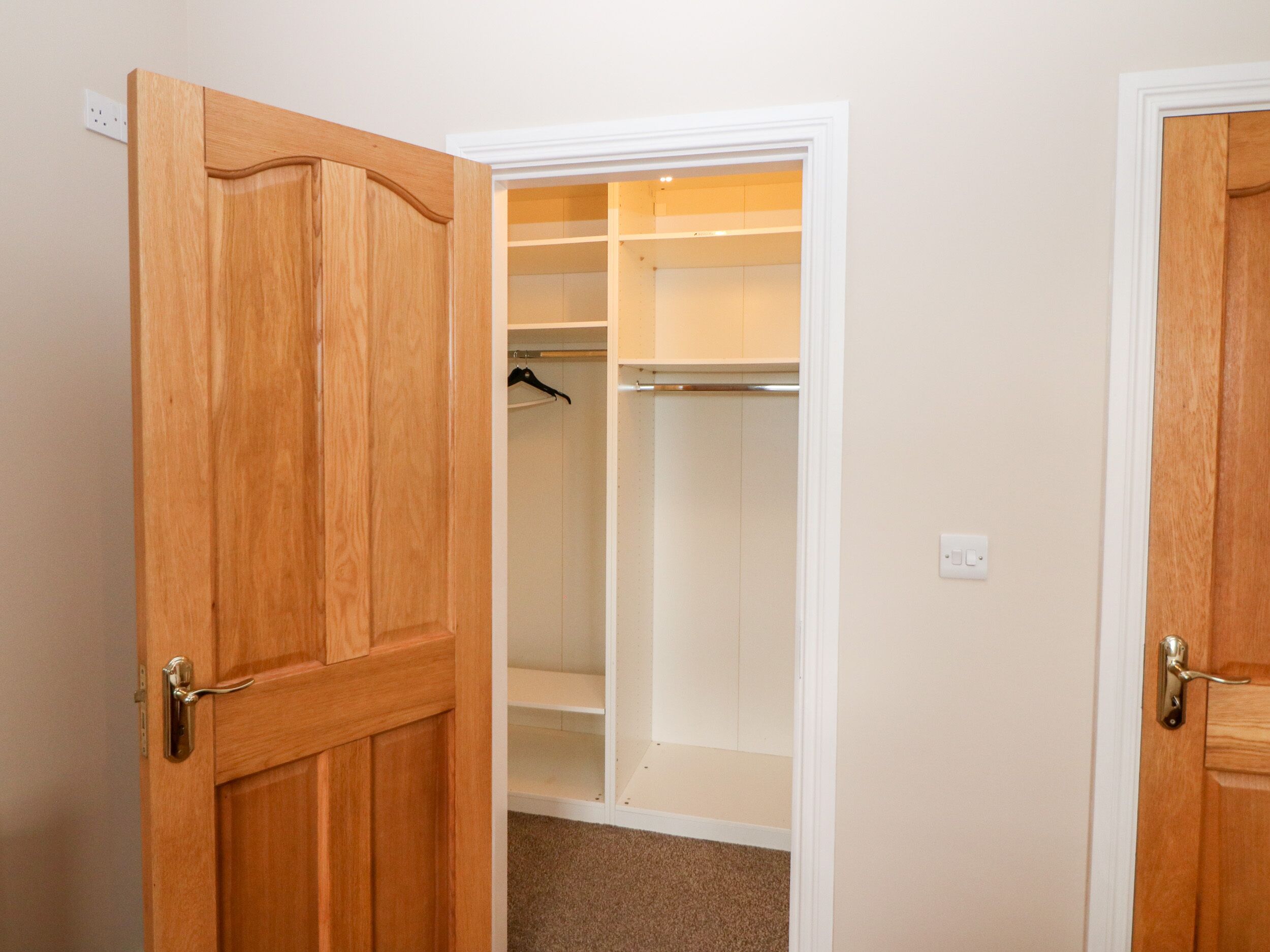 Ein Holzschrank mit weißen Regalen, einer Kleiderstange und einem Teppichboden.