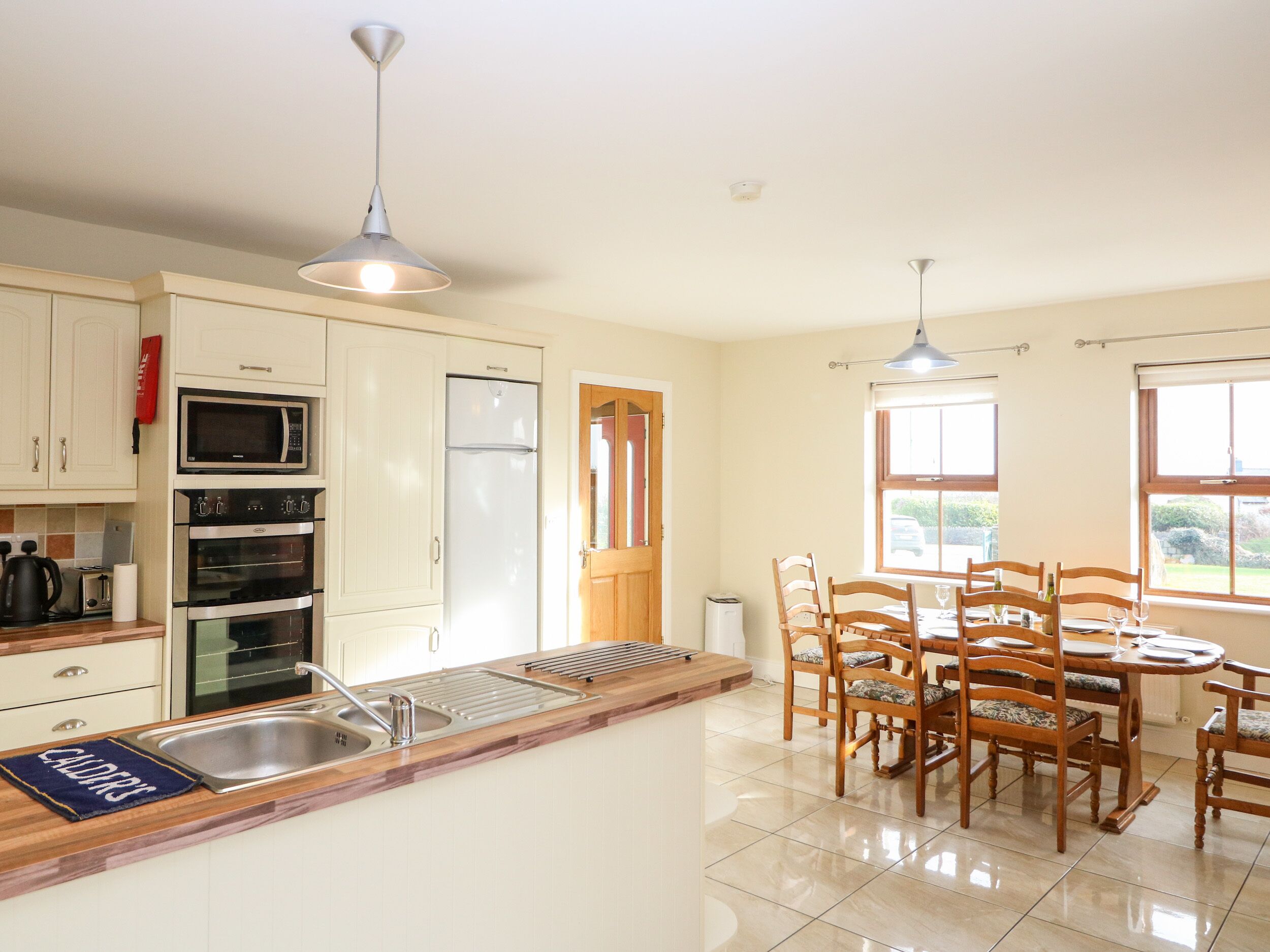 A kitchen with white cabinets, a built-in oven, a microwave, a refrigerator, a sink, and a dining area with wooden chairs and a table.