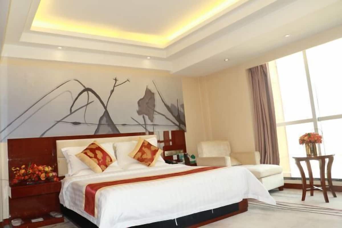 A hotel room with a large bed, a nightstand, a chair, a table, and a large window.