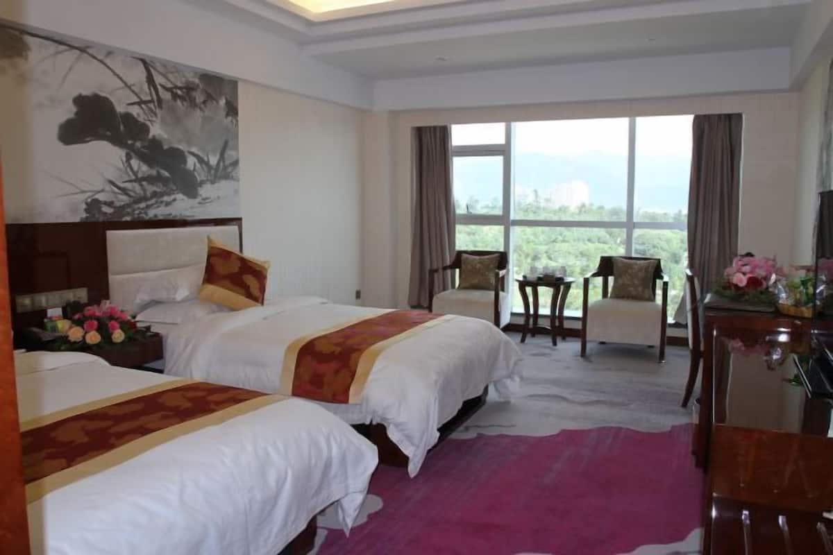 A hotel room with two beds, a large window with a view, a desk with a chair, and a decorative painting on the wall.