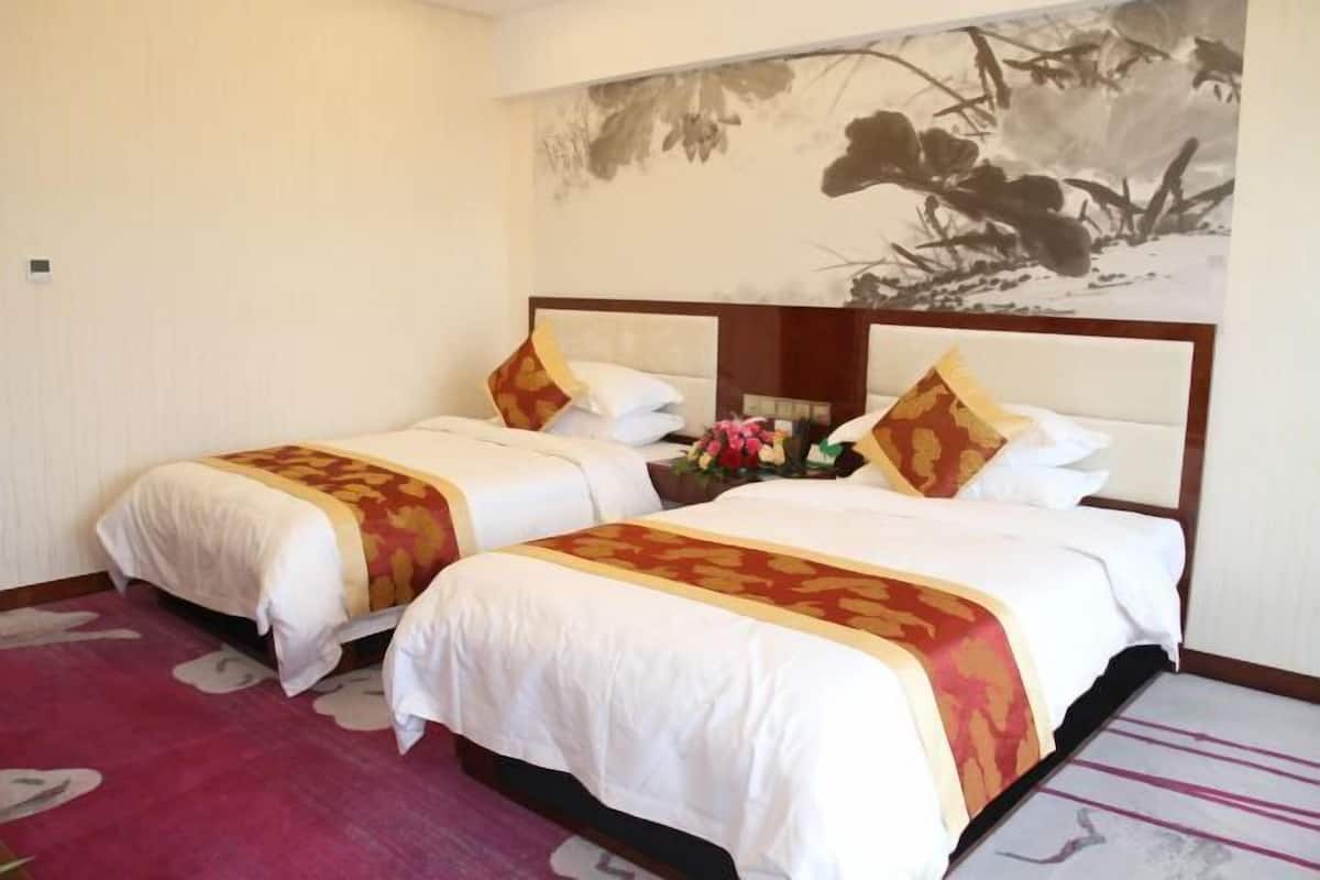 A hotel room with two beds, a large painting on the wall, and a floral arrangement on the bed.