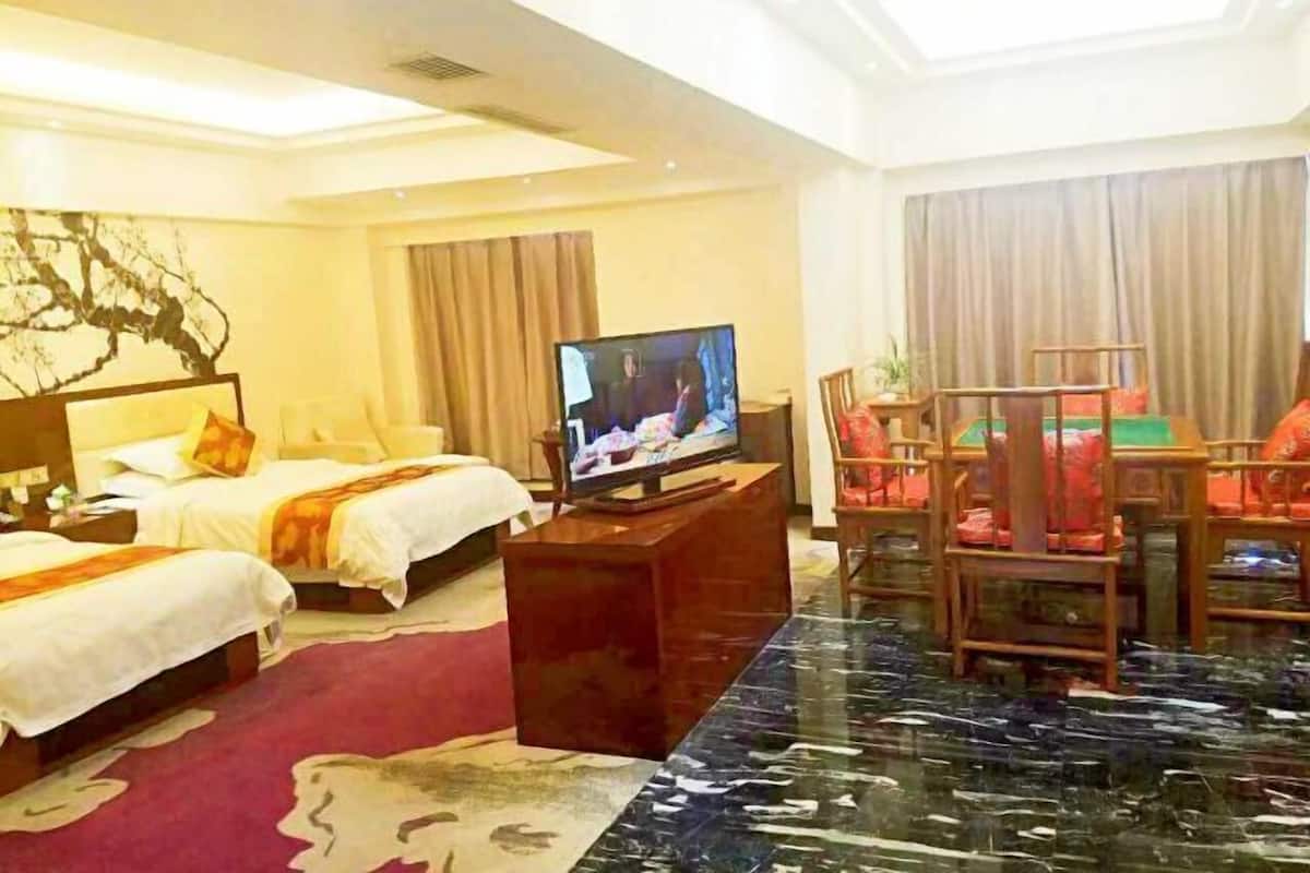 A hotel room with two beds, a television, a dining table with chairs, and a large window with curtains.