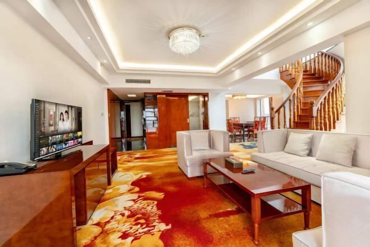 A modern living room with a television, white sofas, a wooden coffee table, and a spiral staircase.