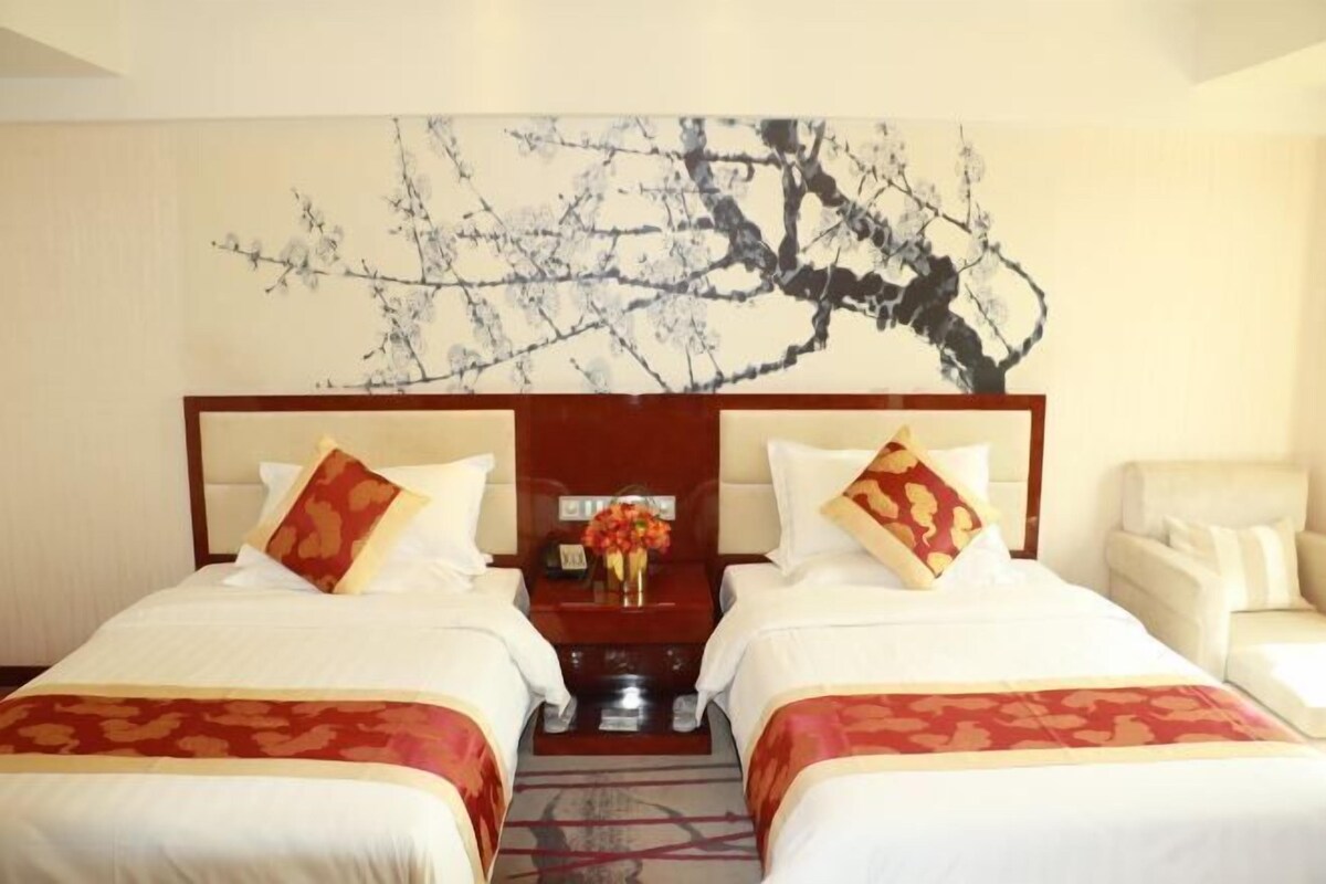 A hotel room with two beds, a nightstand with a vase of flowers, and a large abstract painting on the wall.