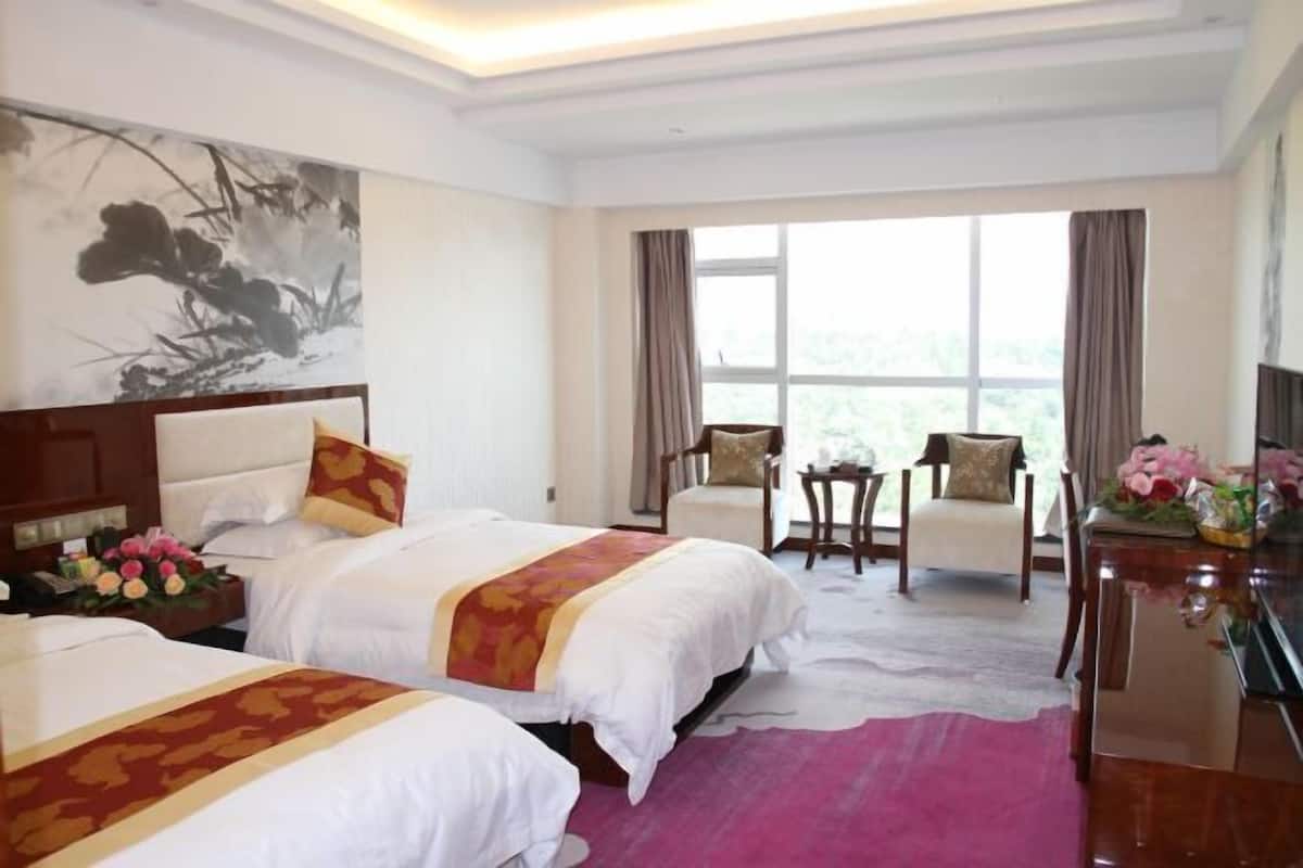 A hotel room with two beds, a desk, a chair, a small table, and a large window.