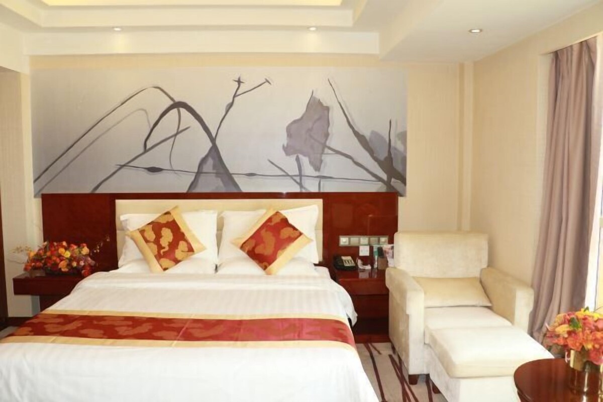 A hotel room with a large bed, a bedside table with a lamp, a chair, and a painting on the wall.