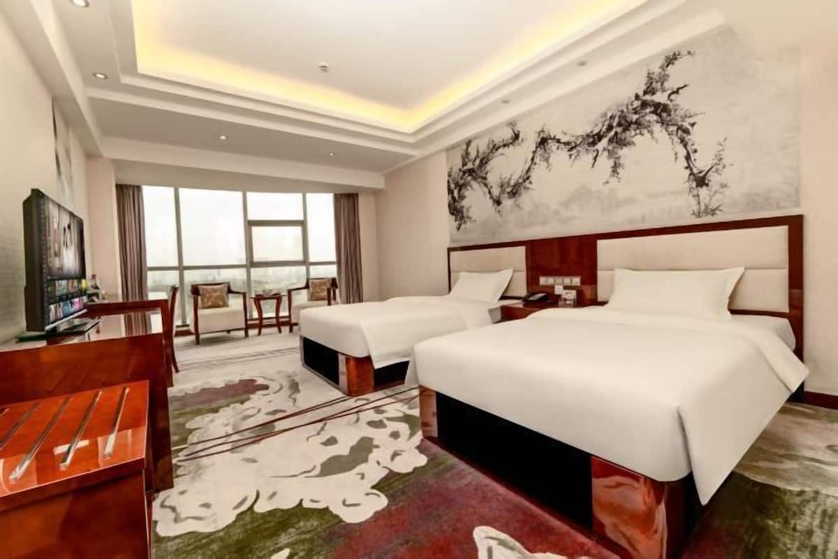 A hotel room with two beds, a desk, a chair, a TV, and a large window.