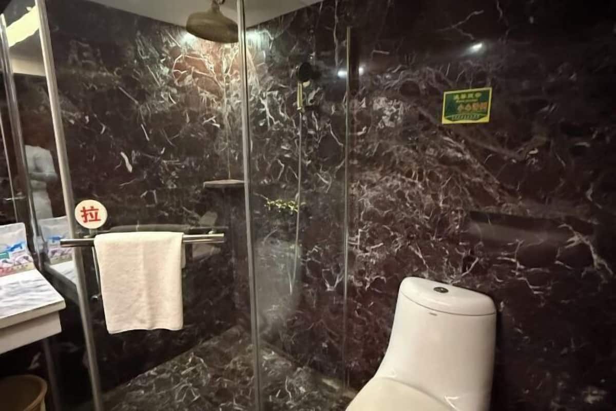 A bathroom with a marble wall, a glass shower enclosure, a toilet, and a towel rack.