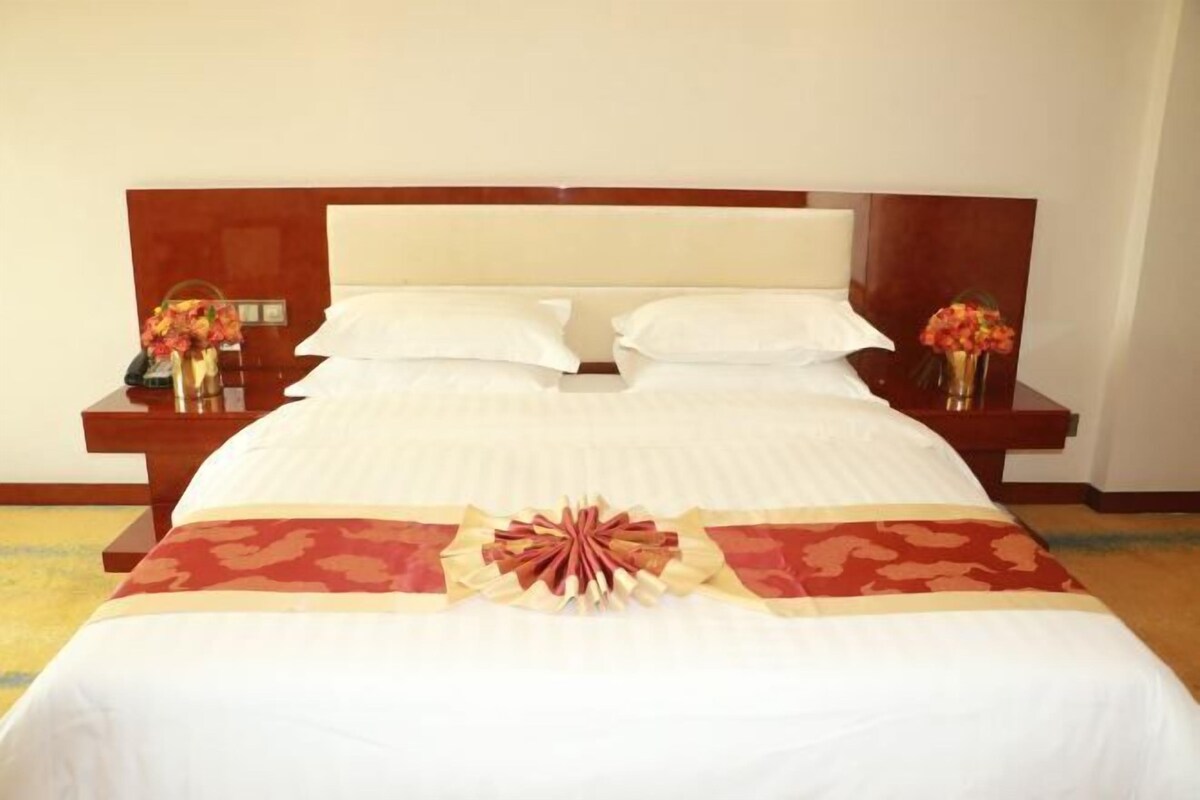 A neatly made bed with a decorative bow, two bedside tables with lamps and vases of flowers, and a wooden headboard.
