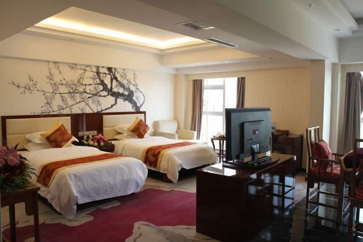 A hotel room with two beds, a desk with a television, and a large window.