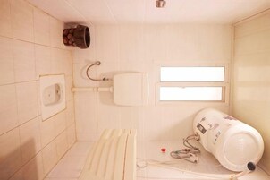 A small, tiled bathroom with a toilet, a hand dryer, and a water heater.
