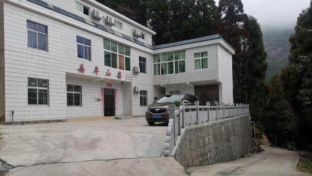 Un edificio de dos pisos con fachada de tejas, un coche estacionado frente a él y un muro de piedra que lleva a la entrada.