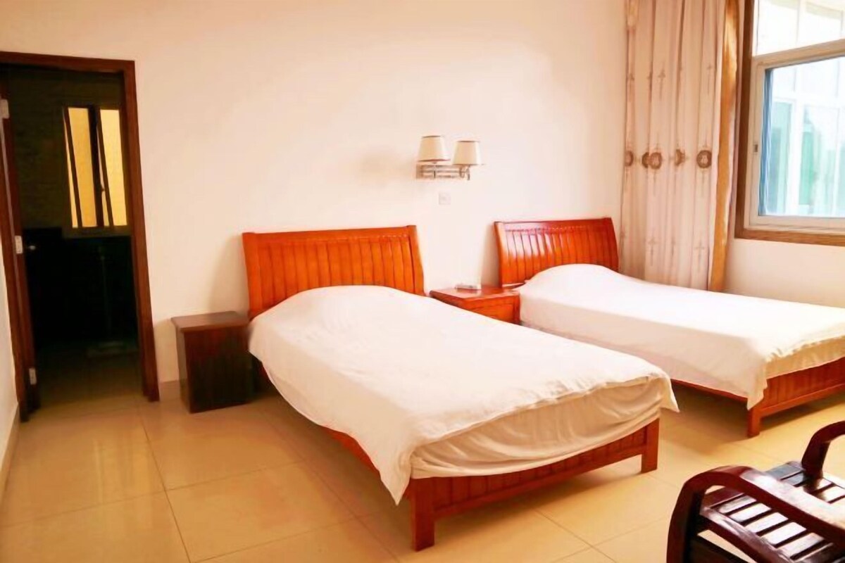 Una habitación de hotel con dos camas de madera, una mesita de noche, una lámpara y un ventanal con cortinas.
