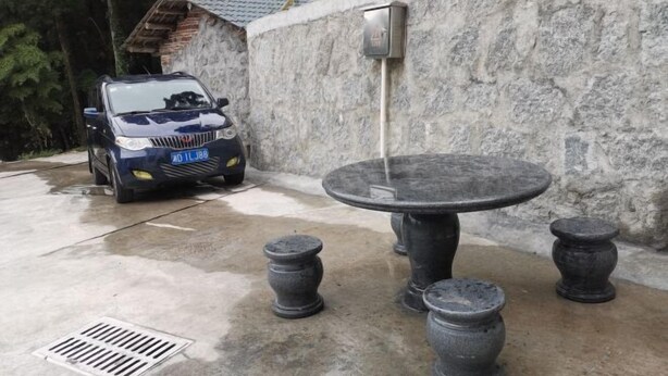 A stone wall with a water feature, a car, and a round table with four legs. - Yue Ping Villa (Hengyang)
